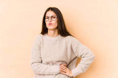 Beyaz tenli, bej arka planda izole edilmiş genç bir kadın. Karaciğer ağrısı, karın ağrısı var..