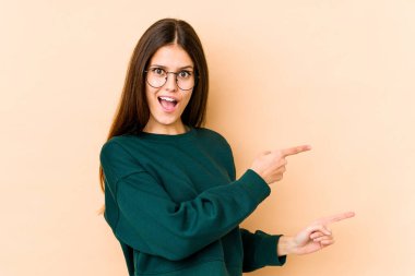 Beyazlı genç bir kadın bej arka planda izole edilmiş. İşaret parmaklarıyla işaret ettiği için heyecanlı..