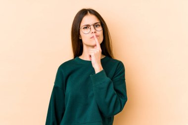 Beyaz tenli genç bir kadın bej arka planda izole edilmiş düşünüyor ve yukarı bakıyor, yansıtıyor, düşünüyor, hayal kuruyor..