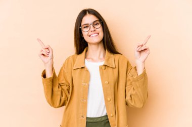 Beyaz tenli genç bir kadın bej arka planda izole edilmiş, farklı kopya alanlarını işaret ediyor, birini seçiyor, parmağıyla gösteriyor..