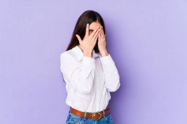 Mor arka planda izole edilmiş genç beyaz kadın parmaklarıyla gözünü kırp korkmuş ve gergin..