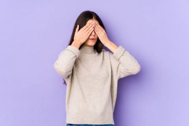 Mor arka planda izole edilmiş genç beyaz kadın elleriyle gözlerini kapatmaktan korkuyor..