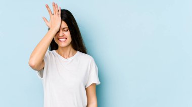 Kafkasyalı genç bir kadın mavi arka planda izole edilmiş bir şekilde bir şeyi unutuyor. Alnına avuç içi ve gözlerini kapayarak vuruyor..