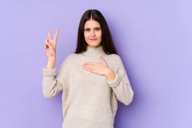 Mor arka planda izole edilmiş genç beyaz kadın yemin ediyor, elini göğsüne koyuyor..
