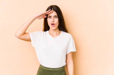 Beyaz tenli genç bir kadın bej arka planda izole edilmiş yüksek sesle bağırıyor, gözleri açık ve elleri gergin tutuyor..