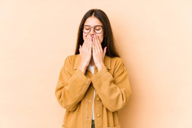 Beyazlı genç bir kadın bej arka planda izole edilmiş bir şekilde bir şeye gülüyor, ağızlarını elleriyle kapatıyor..