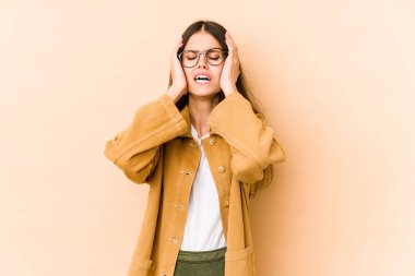 Beyaz tenli genç bir kadın bej arka planda izole edilmiş ağlıyordu, bir şeyden mutsuzdu, acı ve kafa karışıklığı içeriyordu..