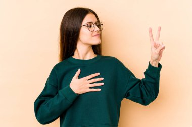 Beyaz tenli genç bir kadın bej arka planda izole edilmiş yemin ediyor, elini göğsüne koyuyor..