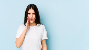 Mavi arka planda izole edilmiş genç beyaz kadın yüksek sesle bağırıyor, gözlerini açık ve ellerini gergin tutuyor..