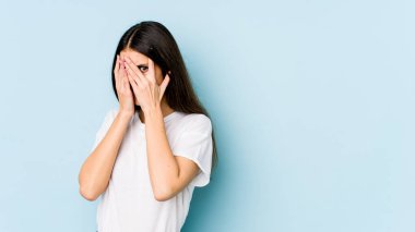 Mavi arka planda izole edilmiş genç beyaz kadın parmaklarıyla gözünü kırp korkmuş ve gergin..