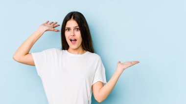 Mavi arka planda izole edilmiş beyaz bir kadın avuç içinde fotokopi alanı tutuyor, el üstünde tutuyor. Şaşırmış ve mutlu..