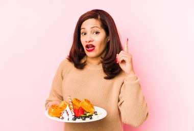 Orta yaşlı, elinde waffle tutan Latin bir kadın. Bir fikri ve ilham konsepti var..