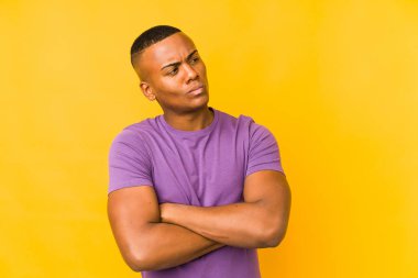 Young latin man isolated on yellow background frowning face in displeasure, keeps arms folded.  
