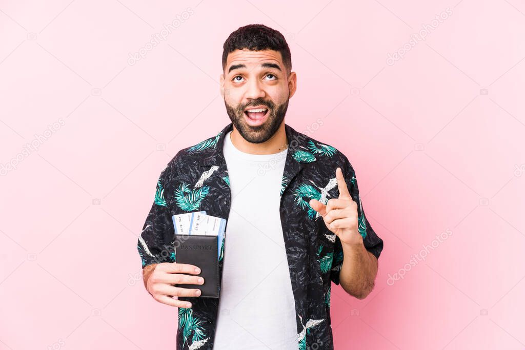 Young arabian cool man holding a boarding passes isolated pointing upside with opened mouth.