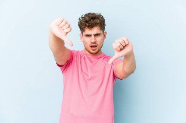 Sarışın, kıvırcık saçlı, beyaz tenli, izole edilmiş, baş parmağını aşağı gösteren ve hoşlanmadığını ifade eden bir adam..