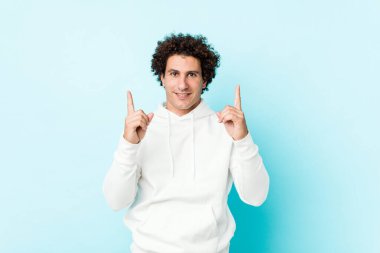 Mavi arka planda genç bir sporcu iki parmağı da boş bir alan gösteriyor..