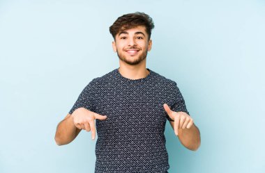 Genç Arap bir adam mavi arka planda izole edilmiş, parmakları aşağıda, olumlu bir his var..