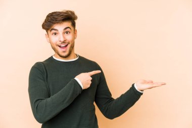 Bej arka planda izole edilmiş genç bir Arap, palmiye üzerinde bir kopya alanı tutarken heyecanlanıyor..