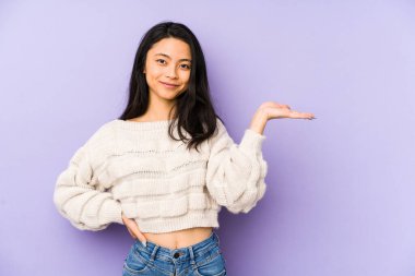 Mor arka planda izole edilmiş genç Çinli kadın bir avuç içinde fotokopi alanı ve belinde bir el daha gösteriyor..