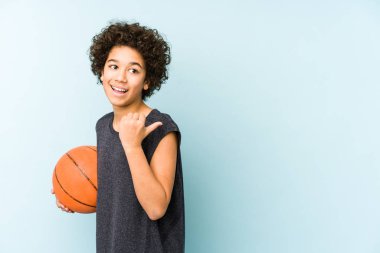 Basketbol oynayan çocuk mavi arka planda izole edilmiş, başparmak uzakta, gülüyor ve kaygısız..
