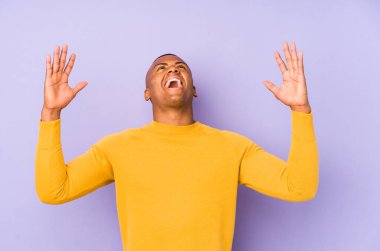 Young latin man isolated on purple background screaming to the sky, looking up, frustrated.