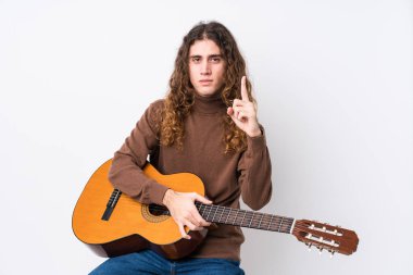 Gitar çalan beyaz bir adam bir numarayı parmağıyla gösteriyor..