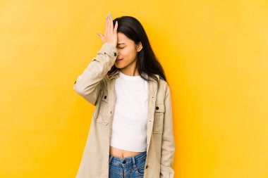 Sarı arka planda izole edilmiş genç Çinli bir kadın bir şeyi unutuyor. Alnına avuç içi ve gözlerini kapatarak tokat atıyor..