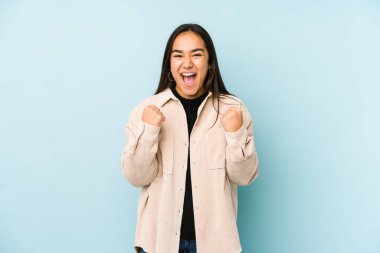 Genç bir kadın mavi bir arka planda yalnız, tasasız ve heyecanlı bir şekilde tezahürat yapıyor. Zafer konsepti.