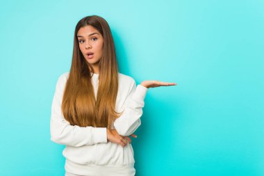 Young slim woman impressed holding copy space on palm.