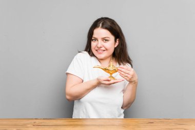 Kafkas kavisli genç bir kadın gri bir arka planda izole edilmiş sihirli bir lambaya arzu soruyor.