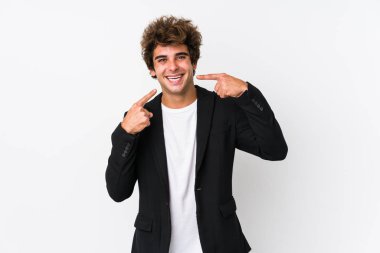 Beyaz arka planda beyaz tenli bir iş adamı yalnız gülümsüyor, parmaklarını ağıza doğrultuyor..