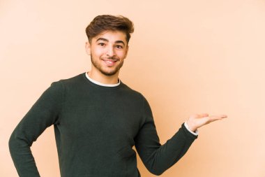 Bej bir arka planda izole edilmiş genç Arap bir adam bir avuç içinde fotokopi alanı ve belinde bir el daha gösteriyor..