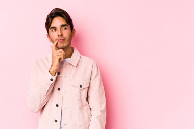 Pembe arka planda poz veren beyaz bir genç şüpheli ve şüpheci bir ifadeyle yanlamasına bakıyor..