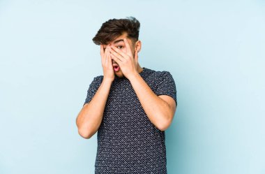 Genç Arap adam mavi bir arka planda izole edilmiş parmaklarıyla gözünü kırp korkmuş ve gergin..