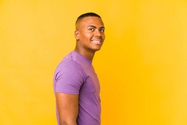 Young latin man isolated on yellow background looks aside smiling, cheerful and pleasant.