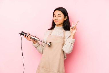 Karıştırıcı tutan genç Çinli kadın yalnız, gülümseyen, neşeli ve keyifli bir kenara bakıyor..