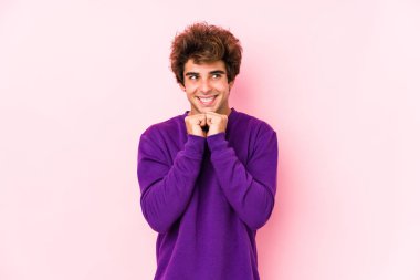 Pembe arka planda genç beyaz bir adam izole edilmiş ellerini çenesinin altında tutuyor, mutlu bir şekilde yana bakıyor..