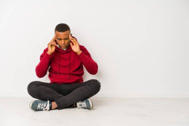 Young latin man sitting on the floor isolated touching temples and having headache.
