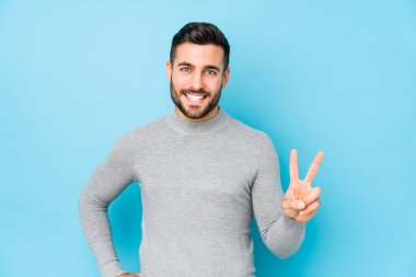 Mavi arka planda, zafer işareti gösteren ve gülümseyen genç, beyaz bir adam..