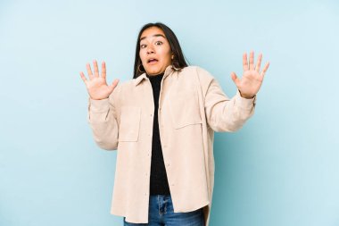 Mavi arka planda izole edilmiş genç bir kadın yakın bir tehlike nedeniyle şoka uğruyor.