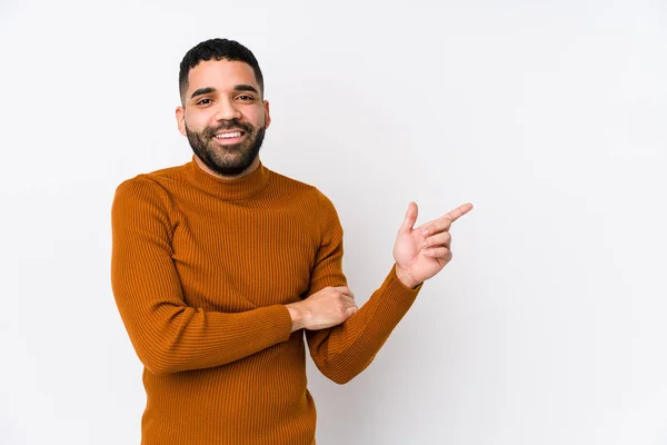Young latin man against a white background isolated smiling cheerfully pointing with forefinger away.