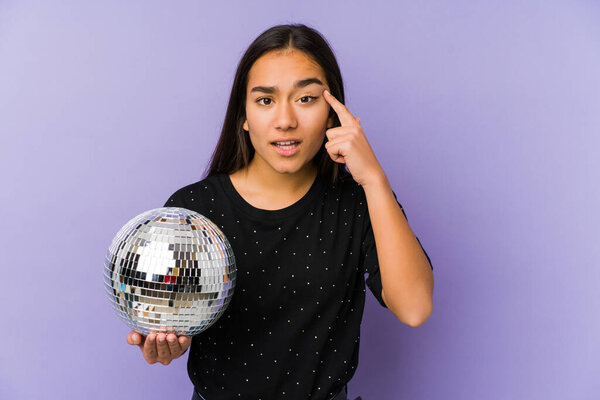 Young asian woman holding a ball party isolated showing a disappointment gesture with forefinger.