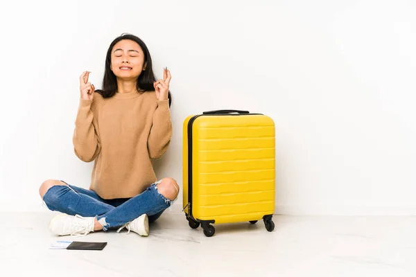 若いです中国人旅行女性座っています上の床にスーツケース隔離された交差指のために運を持っている — ストック写真
