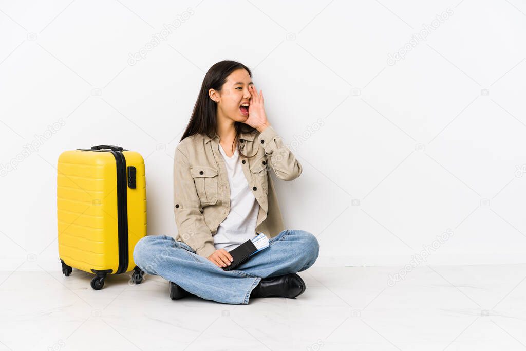 Young chinese traveler woman sitting holding a boarding passes shouting and holding palm near opened mouth.
