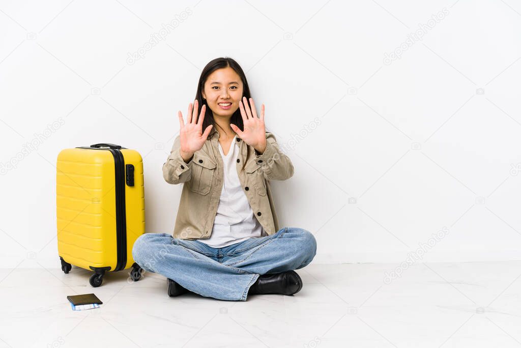 Young chinese traveler woman sitting holding a boarding passes showing number ten with hands.