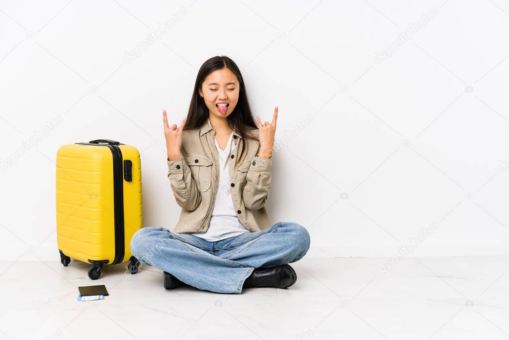 Young chinese traveler woman sitting holding a boarding passes showing rock gesture with fingers