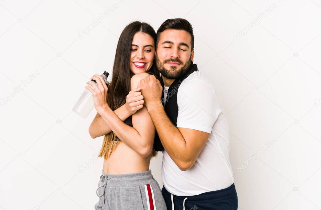 Young caucasian fitness couple isolated hugs, smiling carefree and happy.