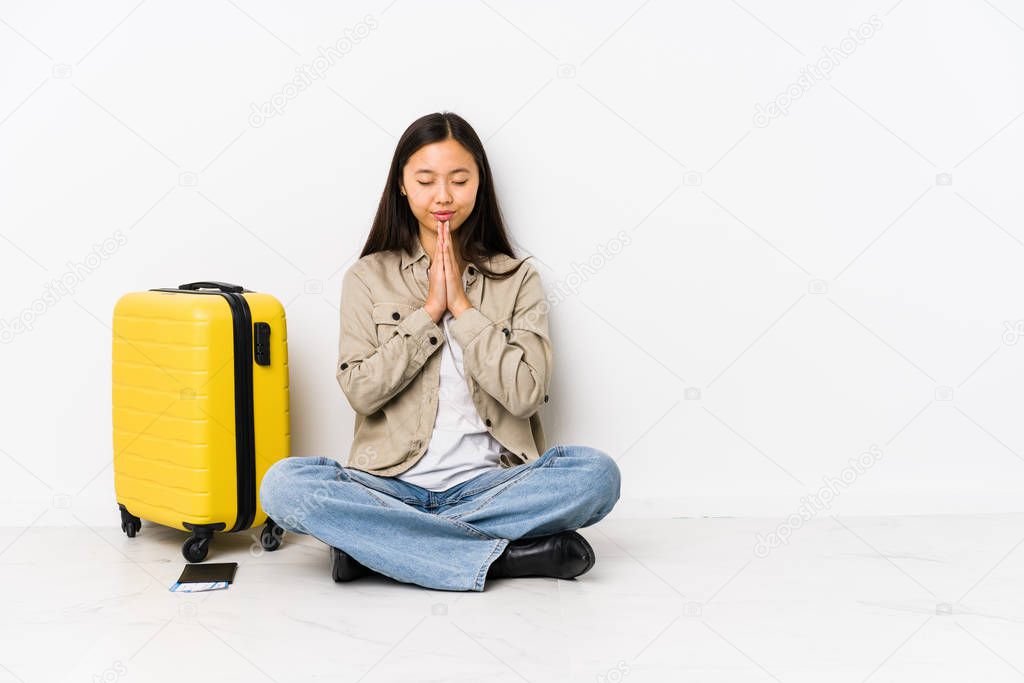 Young chinese traveler woman sitting holding a boarding passes holding hands in pray near mouth, feels confident.