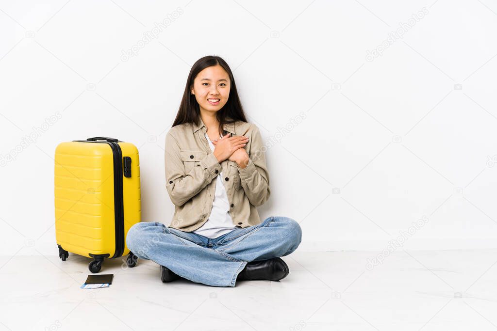 Young chinese traveler woman sitting holding a boarding passes has friendly expression, pressing palm to chest. Love concept.