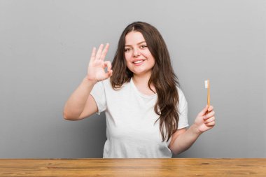 Genç ve cüsseli bir kadın elinde bir diş fırçası tutuyor neşeli ve kendinden emin..